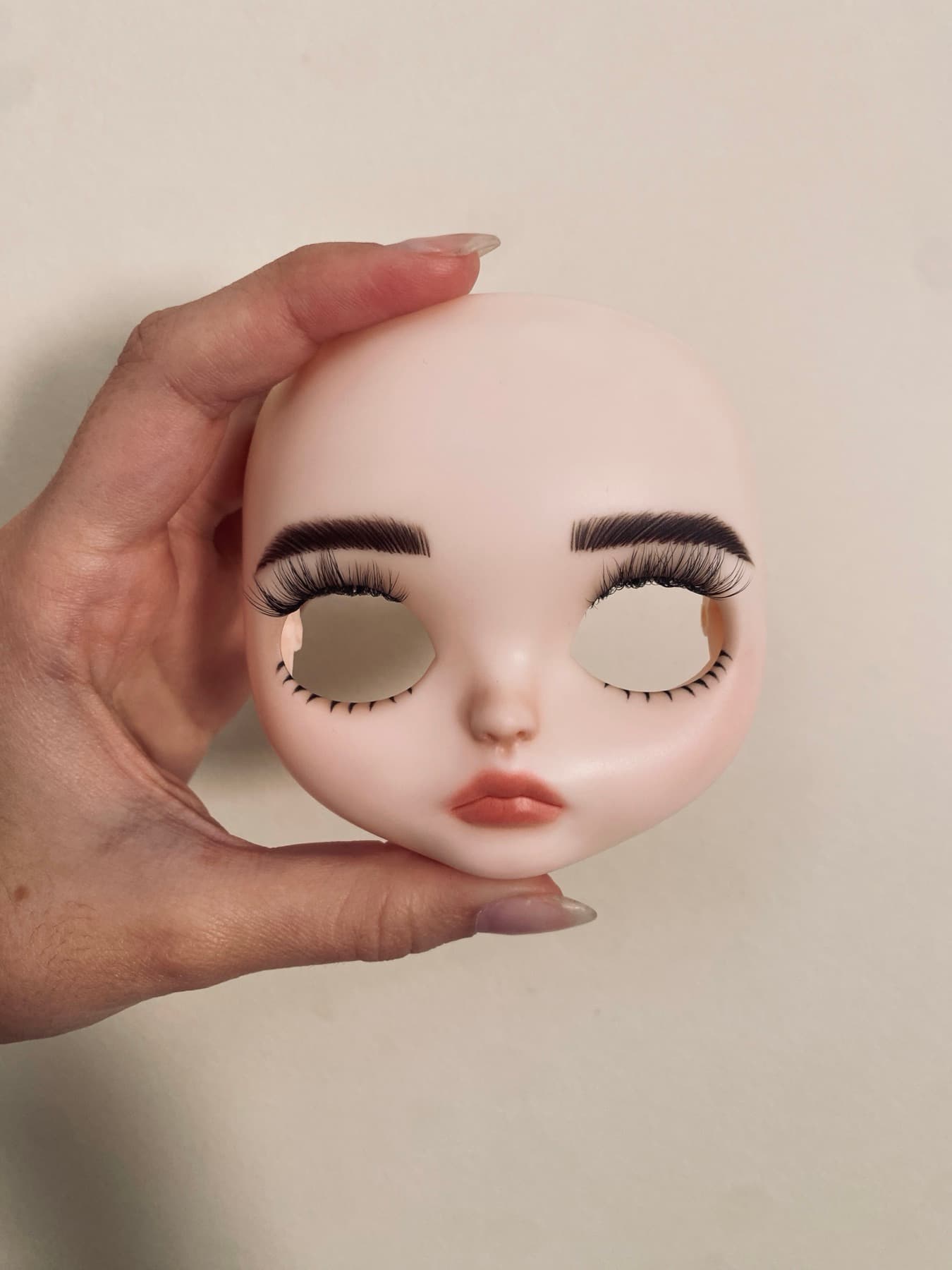A hand holding a freshly painted doll face with brows and lashes set